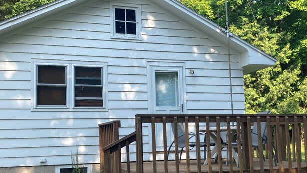 A white two-story house with a wooden deck and a small porch. - Charming 2-bedroom cottage in Fish Creek with AC, heat, WiFi (Fish Creek)