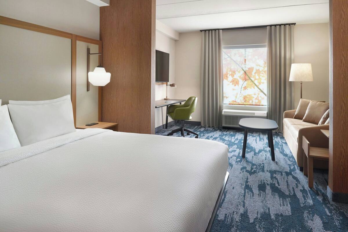 A hotel room with a large bed, a desk with a chair, a sofa, a TV, and a window with curtains.