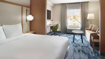 A hotel room with a large bed, a desk with a chair, a sofa, a TV, and a window with curtains.