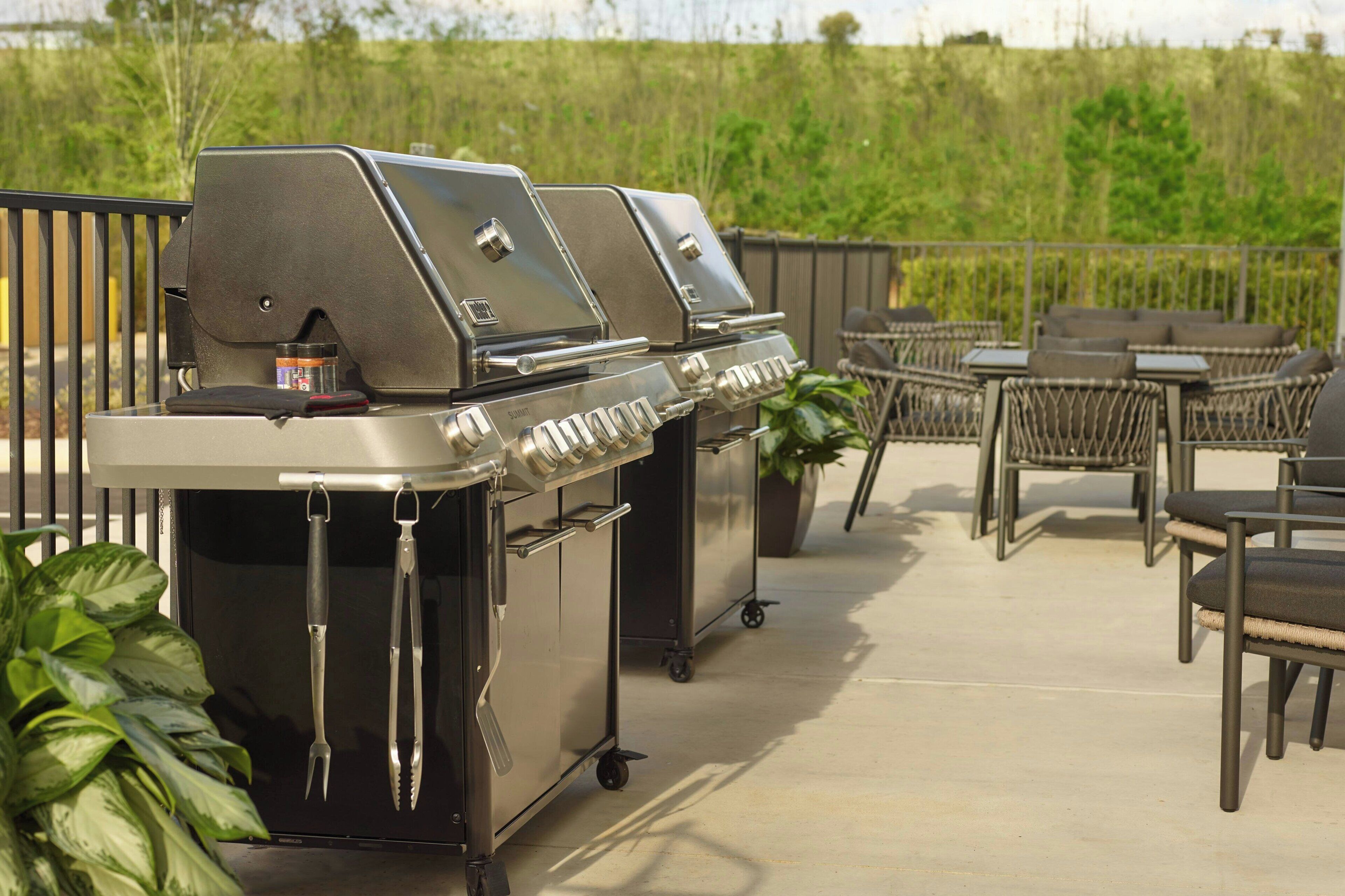 Een terras met een roestvrijstalen barbecue, tuinmeubels en een bloempot.