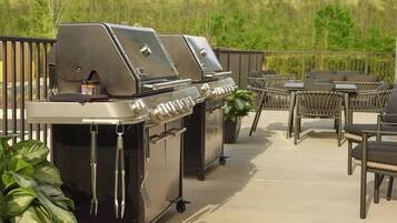 Een terras met een roestvrijstalen barbecue, tuinmeubels en een bloempot.