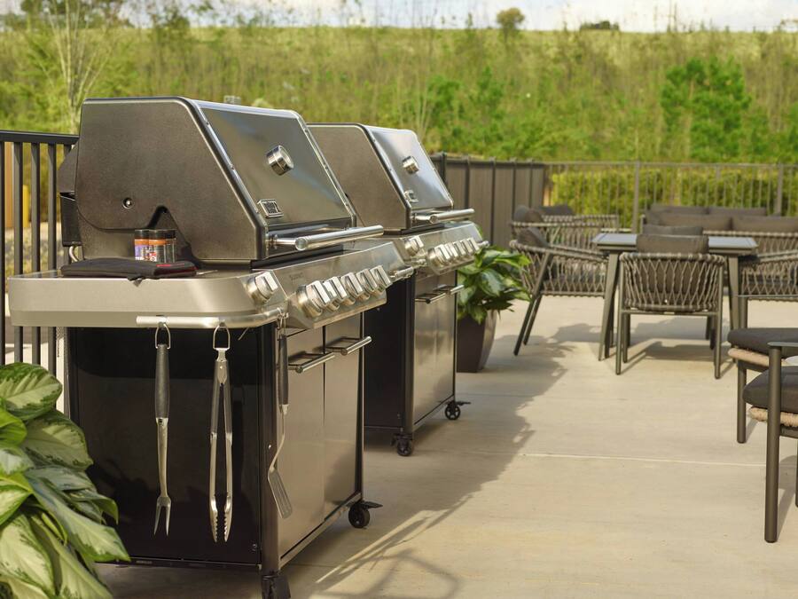 Une terrasse avec un barbecue en acier inoxydable, du mobilier d’extérieur et une plante en pot.