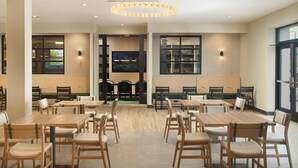 A modern restaurant with wooden tables and chairs, a central seating area, and a large screen on the wall. - Fairfield By Marriott® Inn & Suites Grovetown (Grovetown)