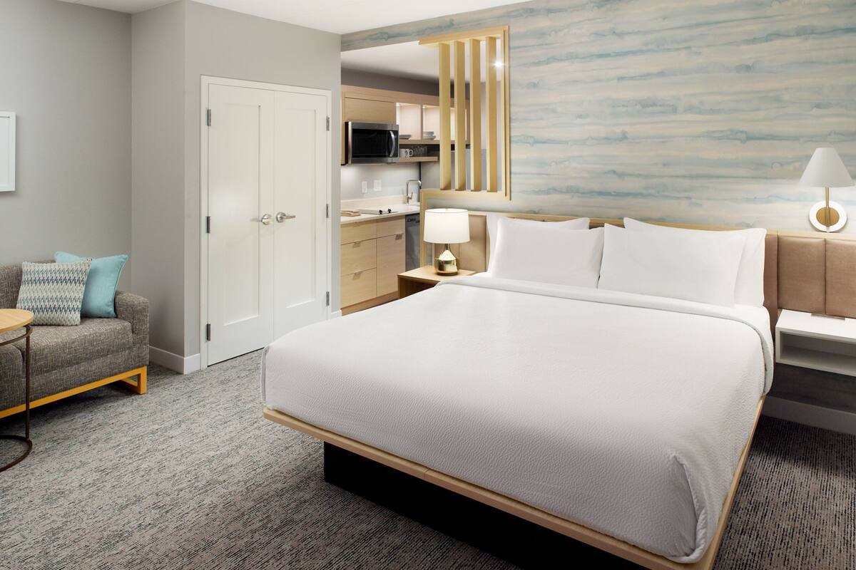Une chambre d’hôtel avec un grand lit, un canapé, un bureau, une lampe, un four à micro-ondes et un coin cuisine.