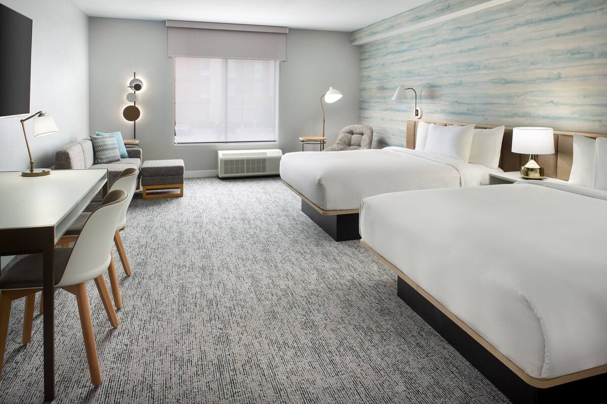 Une chambre d’hôtel avec deux lits, un bureau, une chaise, un canapé et une grande fenêtre donnant sur un beau paysage.