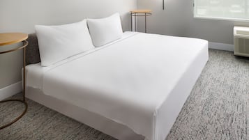 A neatly made bed with white linens, a small round table with a wooden top, and a wall-mounted light fixture.