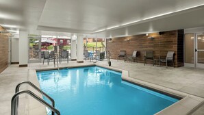 An indoor swimming pool with clear blue water, surrounded by lounge chairs and a glass door leading outside. - Fairfield By Marriott® Inn & Suites Beckley (Beckley)