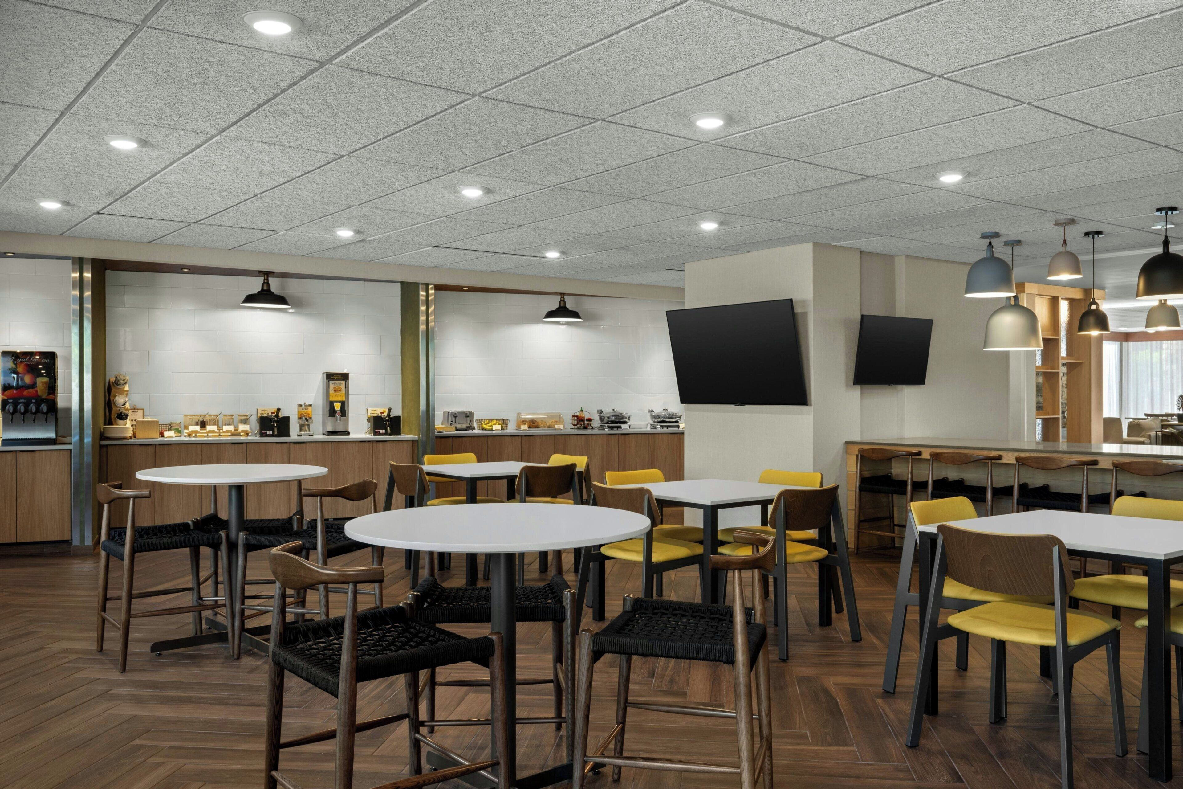 A modern restaurant with round tables and chairs, a counter with a flat-screen TV, and pendant lighting.