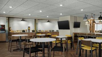 A modern restaurant with round tables and chairs, a counter with a flat-screen TV, and pendant lighting.