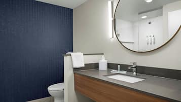 A modern bathroom with a white toilet, a wooden vanity, a large mirror, and a wall-mounted sink.