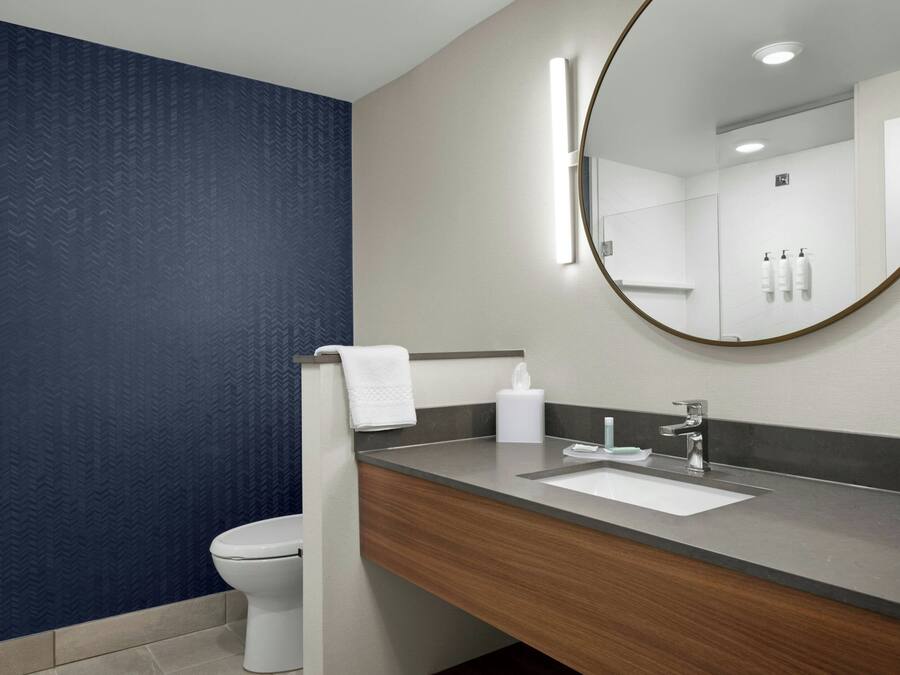 A modern bathroom with a white toilet, a wooden vanity, a large mirror, and a wall-mounted sink.