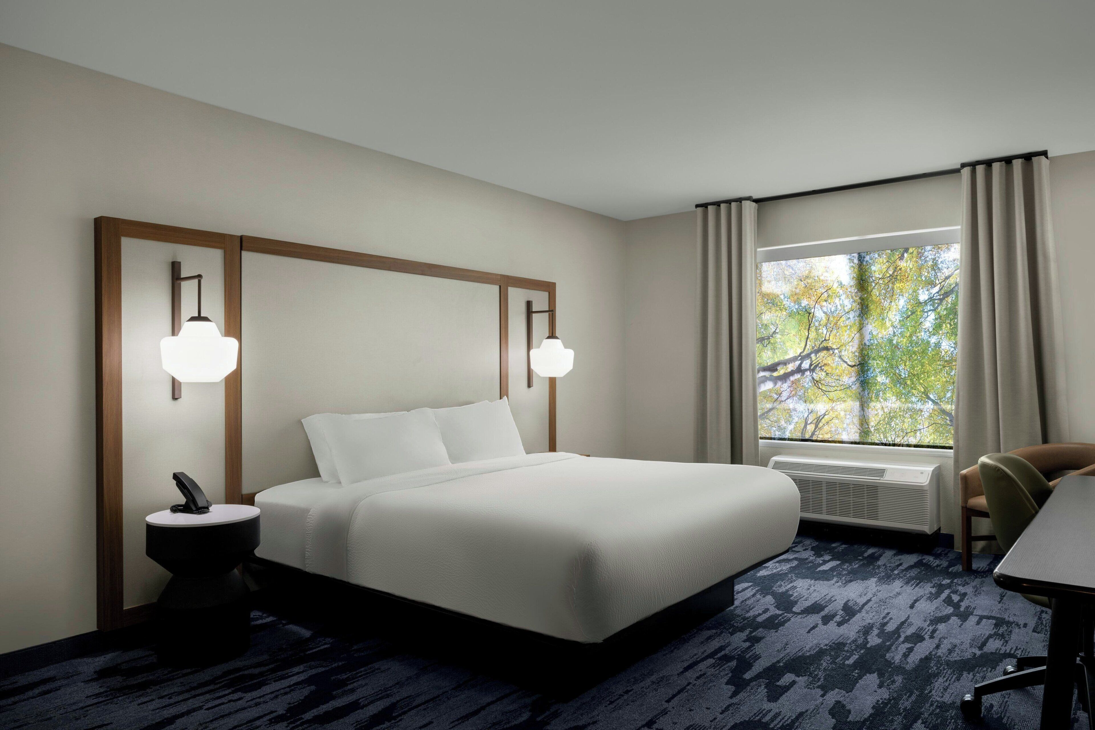 A hotel room with a large bed, bedside lamps, a desk, and a window with curtains.