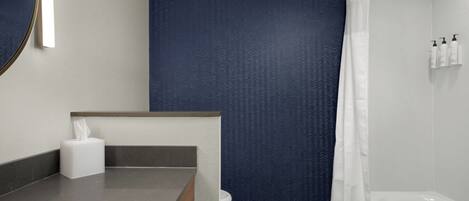 Un baño moderno con un lavamanos gris, un inodoro blanco, una bañera y una pared azul con textura.