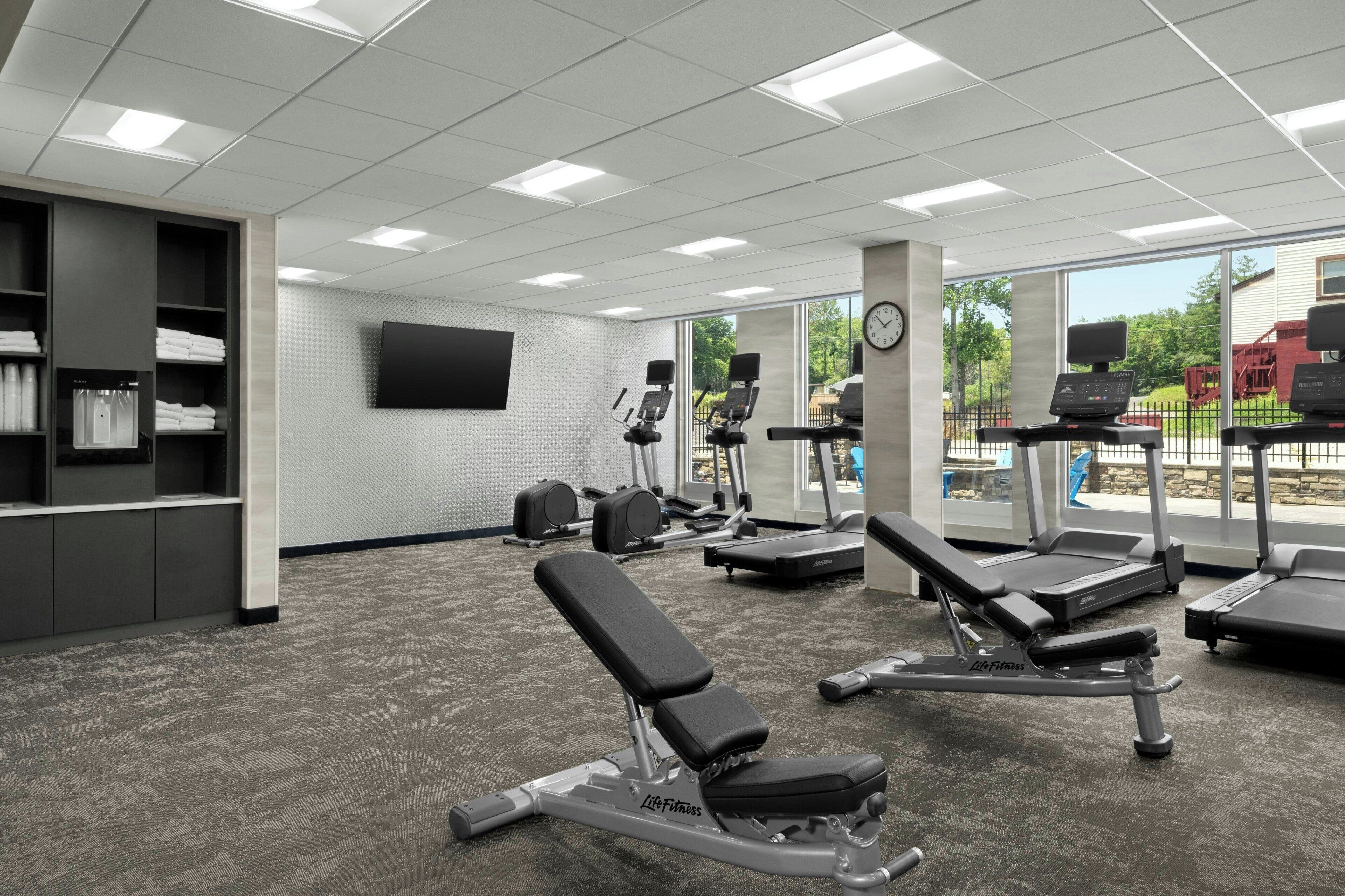 Un gimnasio con cintas de correr, elípticas y una prensa de banca.