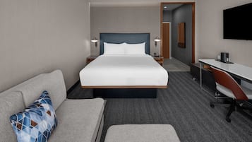 A hotel room with a large bed, a desk, a chair, a sofa, and a TV.