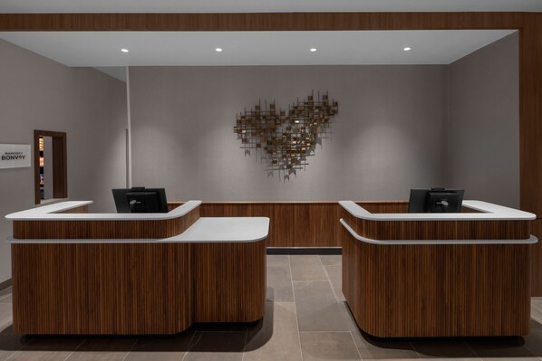 A reception area with two wooden reception desks, a modern wall art piece, and a sign for "Marriott Bonvoy". - Courtyard® By Marriott® Reno Sparks (Sparks)