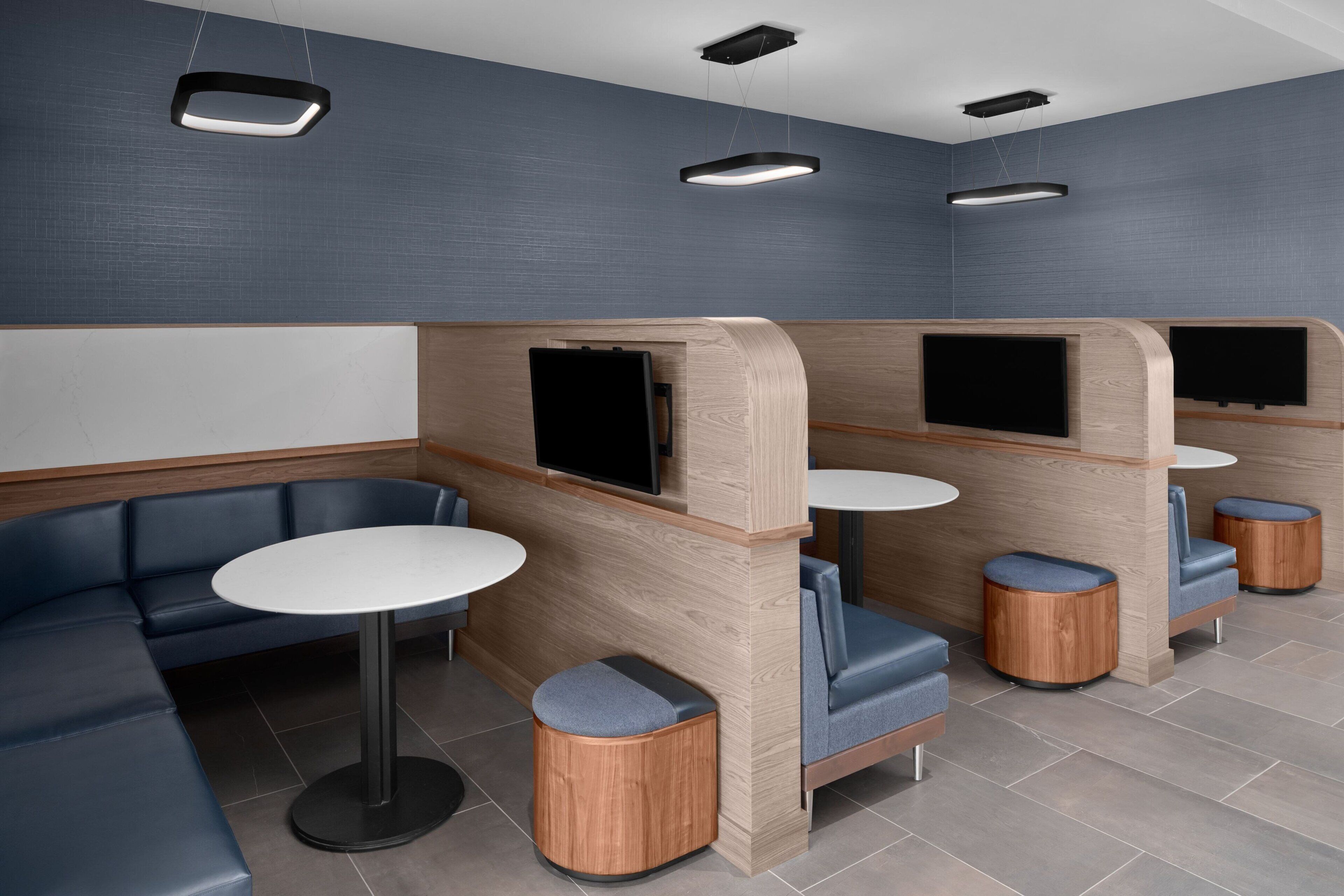 Un área de lounge moderna con disposición de asientos, incluyendo un sofá y mesas, y pantallas de televisión integradas.