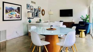 A modern dining area with a round glass table, white chairs, and a wooden base.