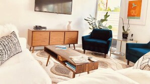 A modern living room with a flat-screen TV, a wooden cabinet, a blue armchair, and a coffee table.