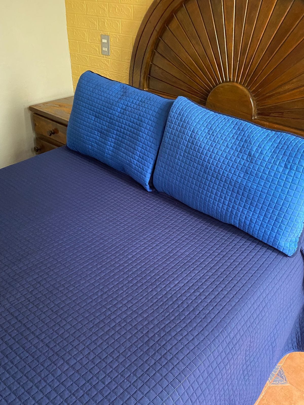 Una cama con una colcha azul acolchada y dos almohadas a juego.