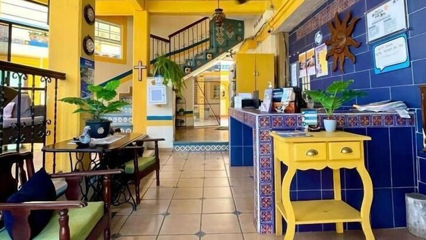 Un hall de hotel con mostrador de recepción, una escalera y un área de descanso con muebles de madera.