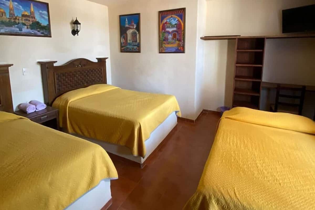 Une chambre d’hôtel avec deux lits, une tête de lit en bois, un téléviseur à écran plat et des œuvres d’art accrochées aux murs.