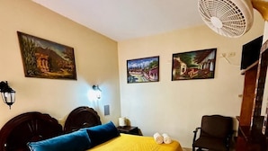 Habitación de hotel con cama, una silla, un ventilador y obras de arte en las paredes.