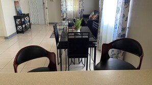 A dining area with a table and chairs, a sofa, a TV mounted on the wall, and a door with a window. - Charming 1-bedroom house with AC, WiFi in welcoming Falmouth (Falmouth)