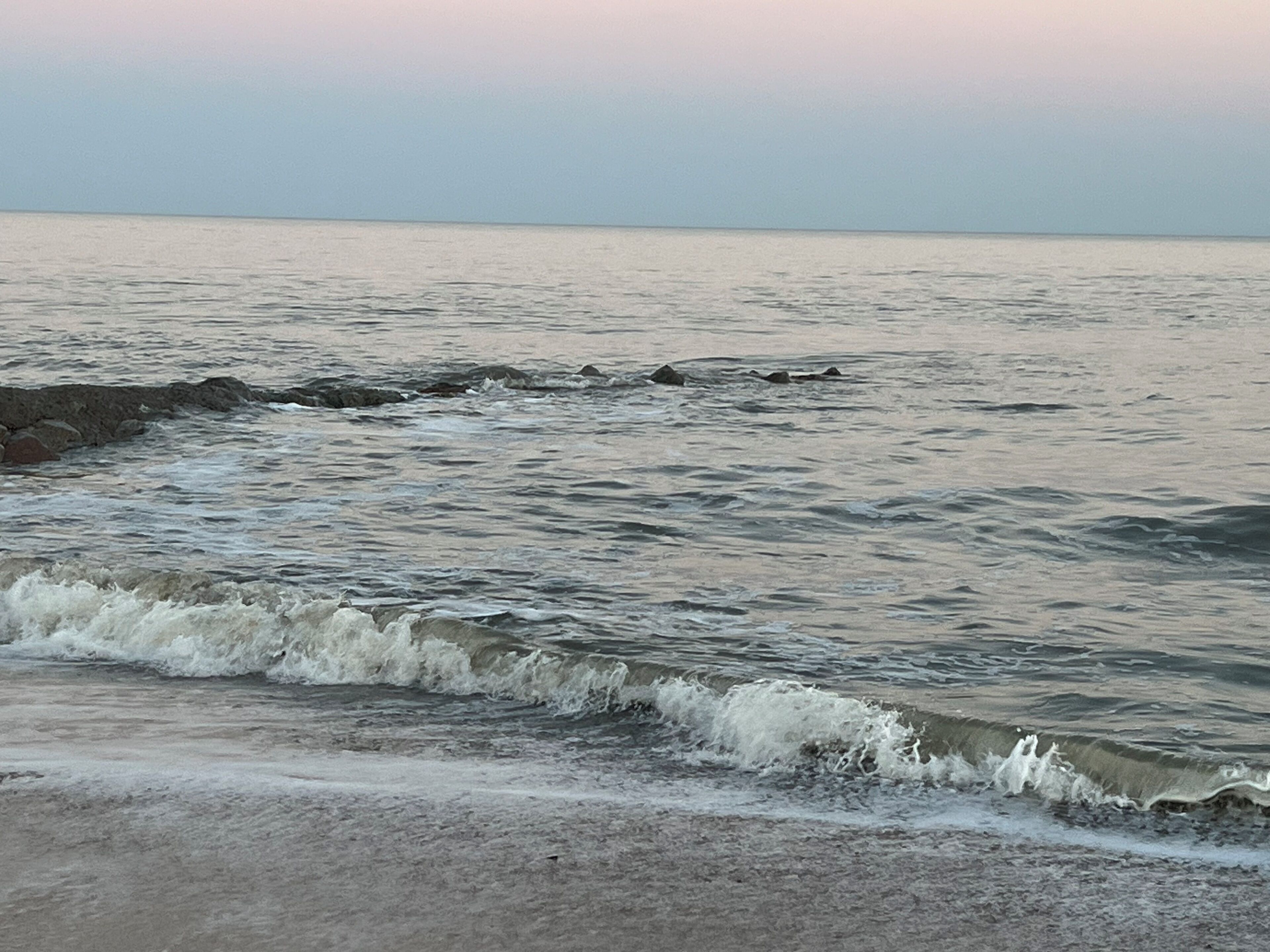A beach with waves crashing onto the shore and a clear sky.
