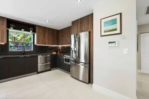 Una cocina moderna con armarios oscuros, electrodomésticos de acero inoxidable y una ventana con vistas a la vegetación.