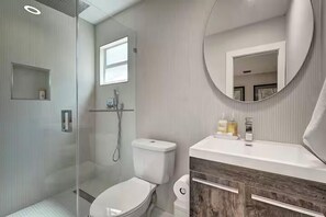 Un baño moderno con ducha de vidrio, inodoro y tocador con espejo.