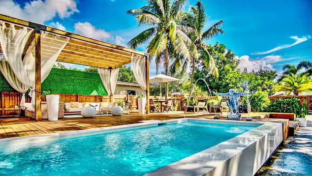 A pool area with a wooden deck, lounge chairs, and a covered seating area. - Tree House (Fort Lauderdale)