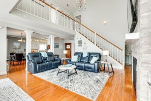 A spacious living room with a large blue sectional sofa, a round coffee table, and a fireplace. A staircase with a wooden railing leads to an upper level. - Waterfront Bliss: Wheeler Lake Retreat w/ Dock! (Athens)