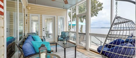 A sunroom with a glass door, a ceiling fan, a hanging chair, and a view of the lake.
