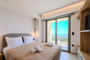 A modern bedroom with a bed, a TV, and a view of the sea.