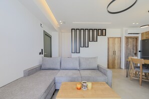 A modern living room with a grey sectional sofa, a wooden coffee table, and a dining area with a wooden table and chairs.