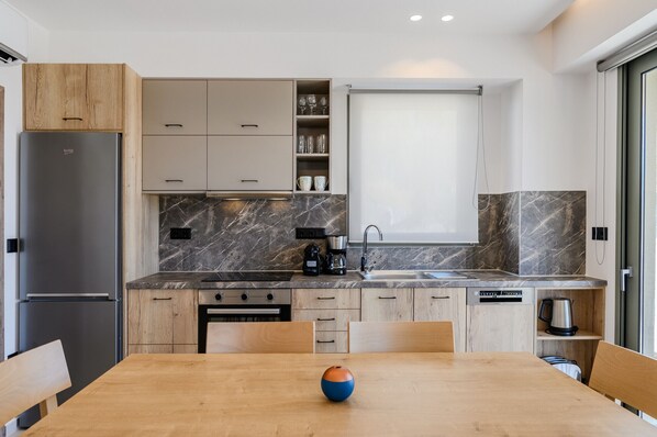 A modern kitchen with a marble countertop, wooden cabinets, and a dining area with a table and chairs.