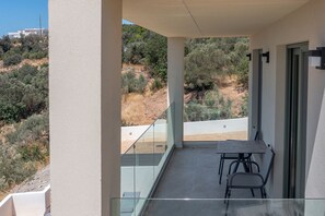 A balcony with a table and chairs, overlooking a hilly landscape with vegetation and a distant building. - Katerina2,Swimming pool,Near beach,Taverns (Mariou)