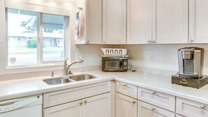 A kitchen with white cabinets, a stainless steel sink, a microwave, and a coffee maker. - Sunny Hilo Home w/ Game Room: Walk to Golf Course! (Hilo)