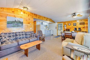 A cozy cabin interior with a wooden wall, a sofa, a dining table, and a kitchen area.