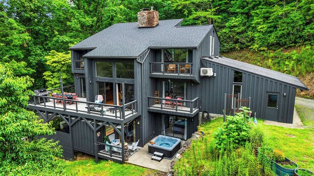 A modern two-story house with a balcony, a hot tub, and a deck area. - Luxe Mountain Home: Hot Tub, Sauna, Firepit, Games (Black Mountain)