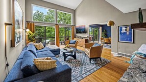 A spacious living room with a large sofa, a coffee table, and a dining area with chairs and a table. - Luxe Mountain Home: Hot Tub, Sauna, Firepit, Games (Black Mountain)