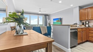 Une cuisine moderne avec des meubles en bois, un coin repas doté d’une table et de chaises en bois, et une vue sur l’océan grâce à de grandes fenêtres.