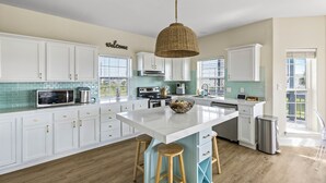 A spacious kitchen with white cabinets, a large island with stools, a hanging light fixture, and a view of the outdoors.