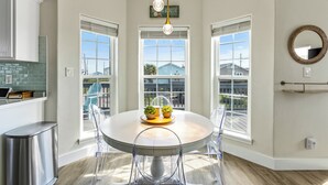 A dining area with a round table, clear chairs, and a view through large windows.