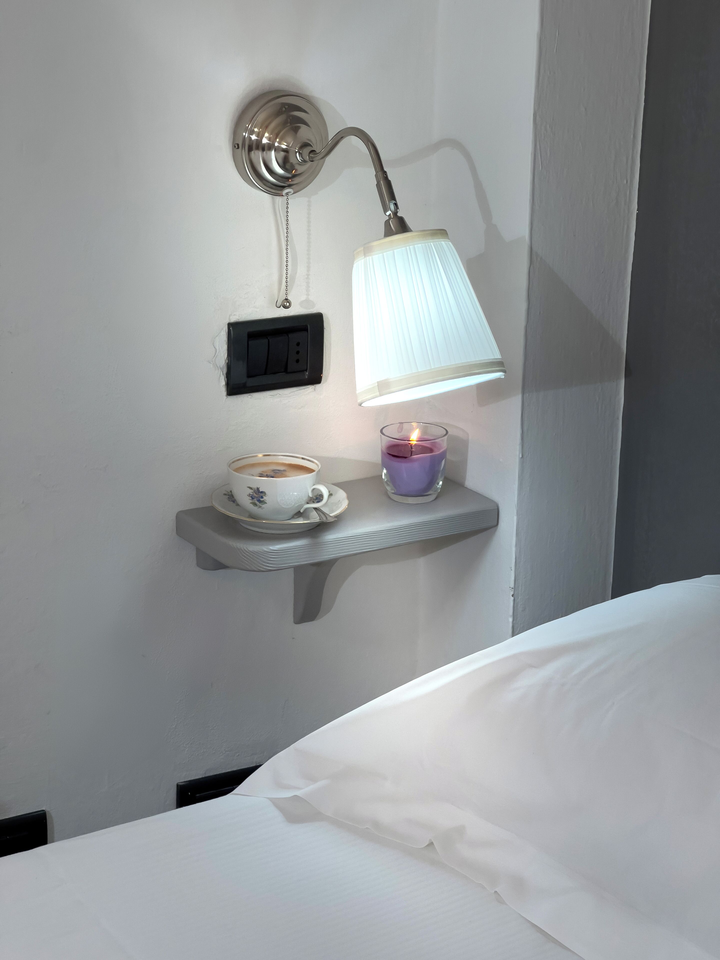 Een nachtkastje met een koffiekop, een kaars en een wandlamp.