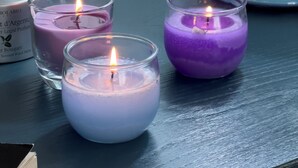 Drie brandende kaarsen in glazen houders op een tafel, een witte keramieken pot met blauwe motieven, en een decoratieve wand met blauw-witte bloemendesigns.