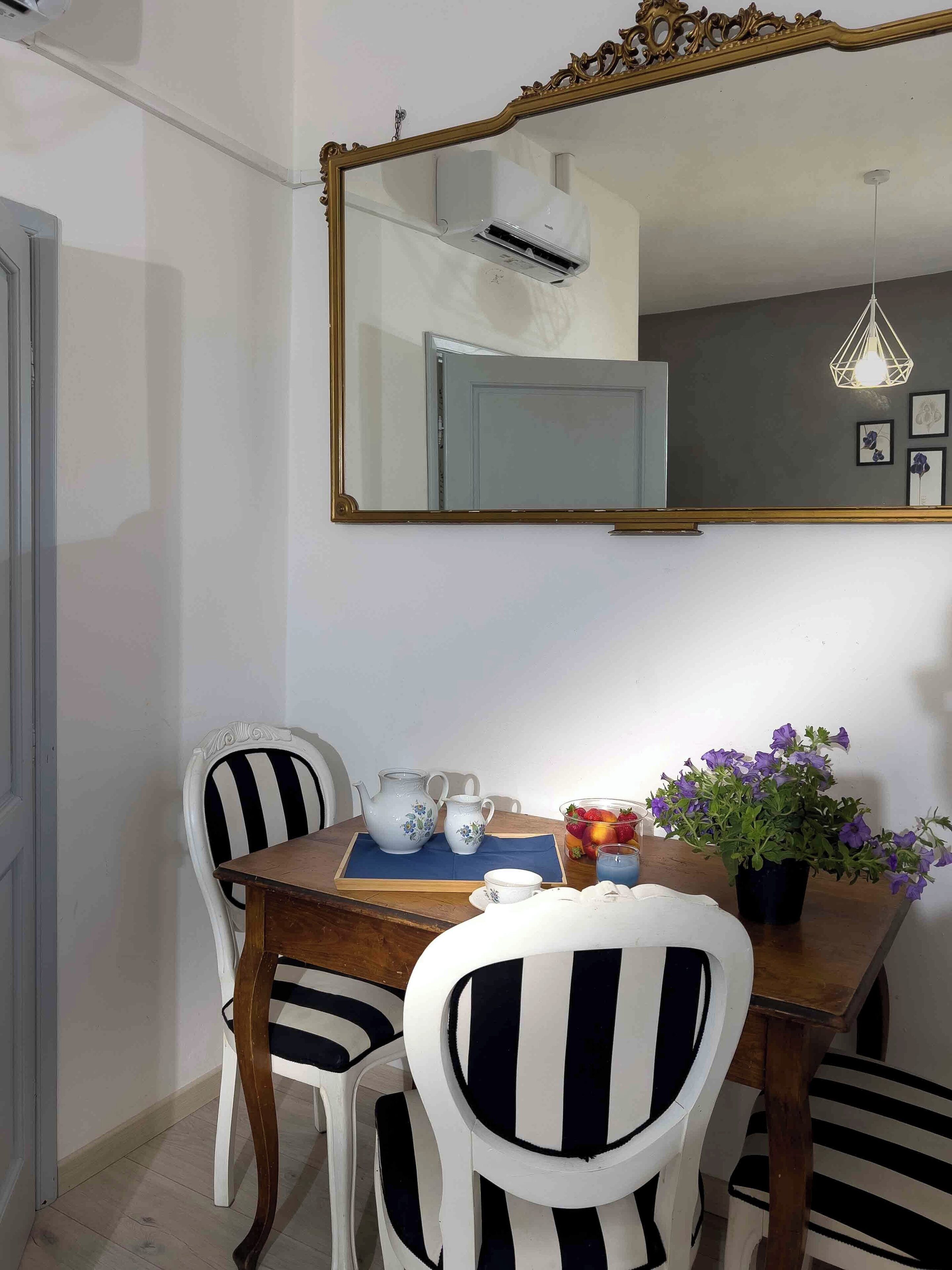 A dining area with a wooden table, two striped chairs, a mirror, and a potted plant.