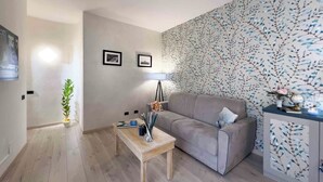Een moderne woonkamer met een grijze bank, een houten salontafel en behang met een patroon.