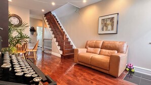 Una sala de estar con escalera de madera, un sofá de cuero marrón y un comedor con sillas y mesa de madera.